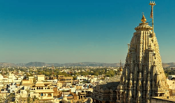 A tall, intricately carved temple spire stands against a clear sky, overlooking a cityscape.