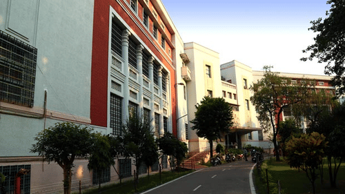 A modern, multi-story white and red building with large windows and a clean pavement leading to the entrance.