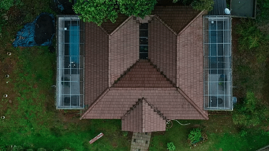 An aerial shot shows a building with a unique M-shaped roof, surrounded by lush greenery. - Abad Brookside Lakkidi, Wayanad