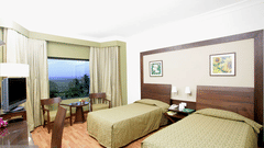 A bedroom with twin beds  at The Retreat Hotel and Convention Centre Madh Island Mumbai, with a table and chairs.