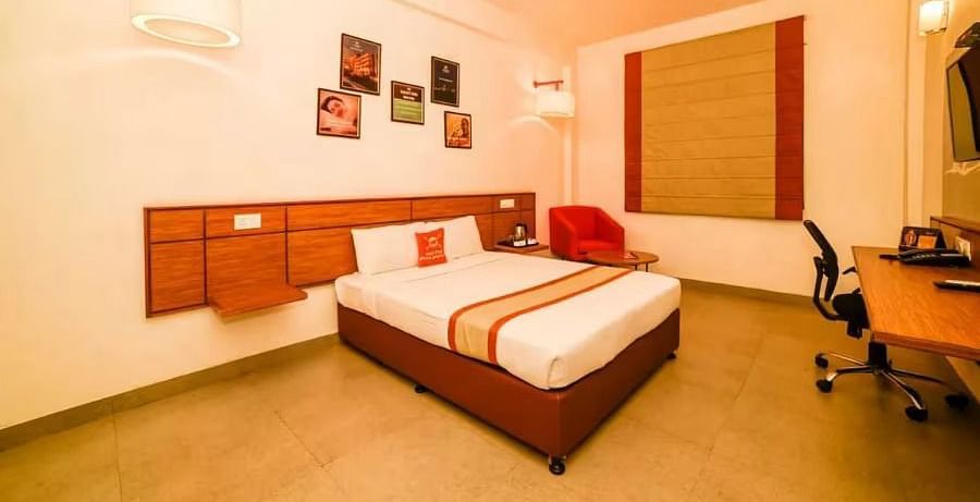 Well-lit hotel room with a double bed, wooden furniture, and wall art - Max Hotel Prayagraj