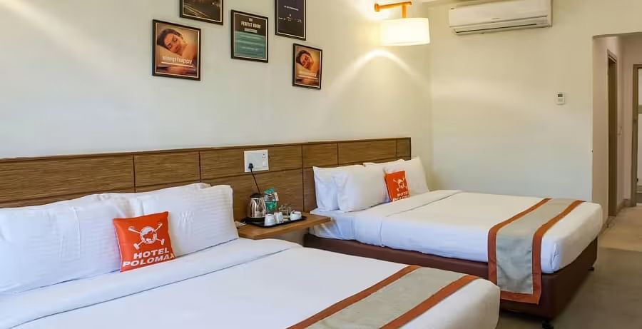 A bright, modern hotel room with twin beds, a wooden headboard, and decorative wall paintings - Max Hotel Prayagraj.