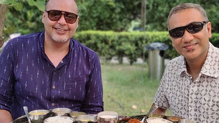 Two middle aged men sitting in an open dining area in a garden with a wide spread of delicious food items served in front of them - Ivory Destinations