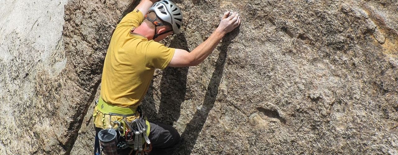 An image of a man climbing rock with having metal locks tied to his waist