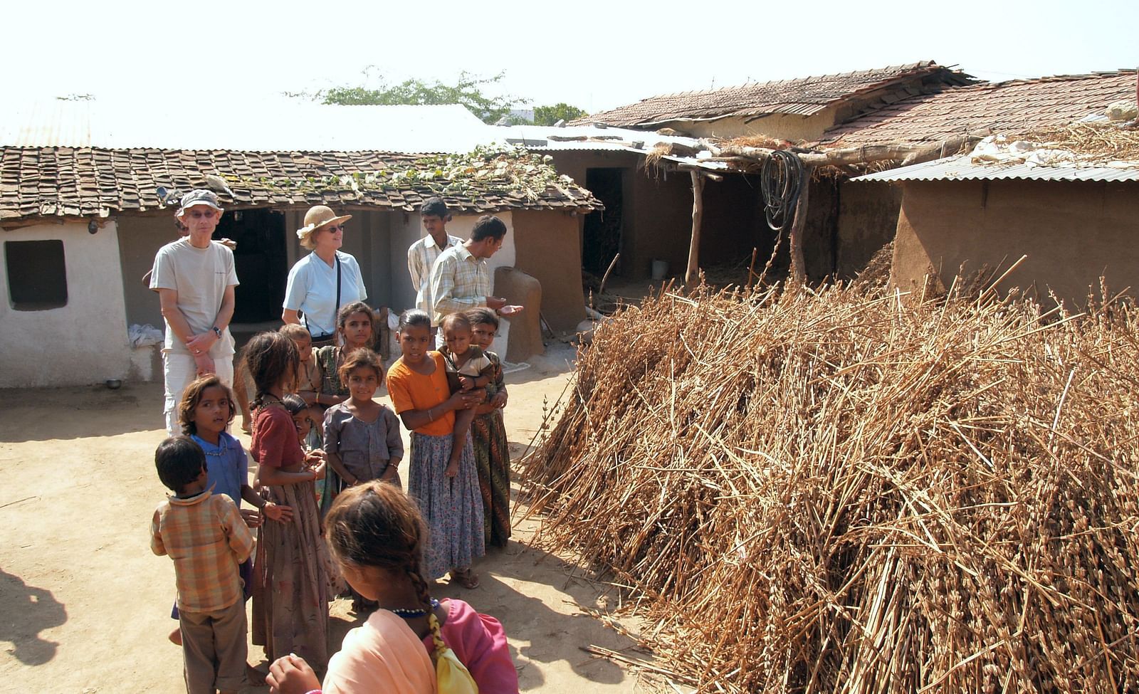 A group of people including adults and children standing near a pile of dried plants- Shahpura Bagh.