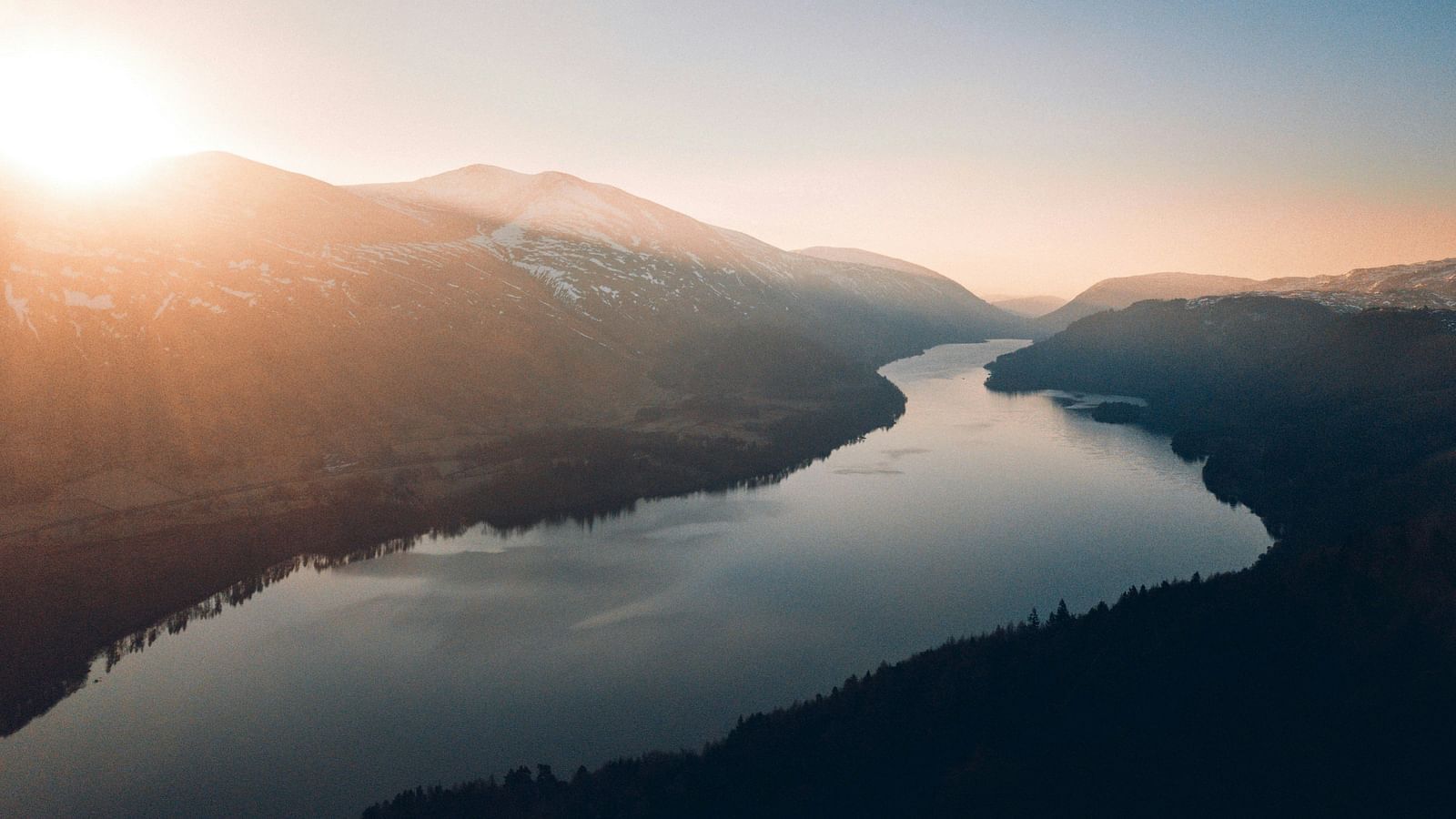 Serene river winding through a forested valley at sunset.