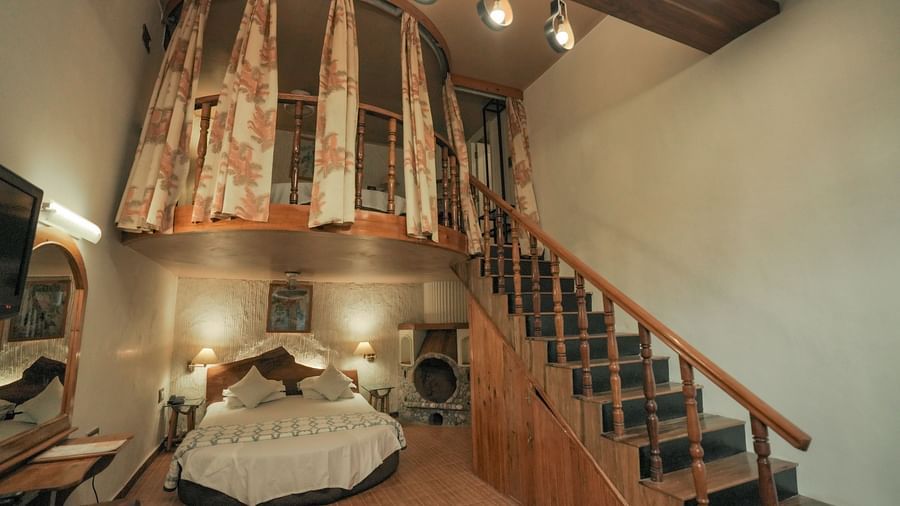 A bedroom with a bed, a rug, and warm lighting, interior setting with wooden elements and stairs - The Den Corbett Resort & Spa, Kumeria.