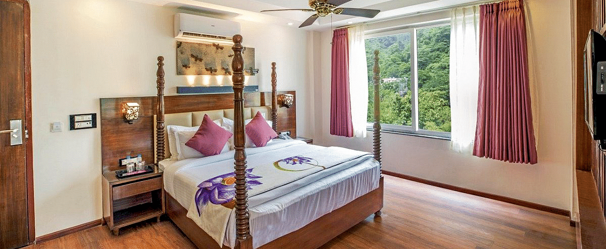 A comfortable double bed with a ceiling fan right above it on a false ceiling and a window besides it at Regenta Inn DLS.