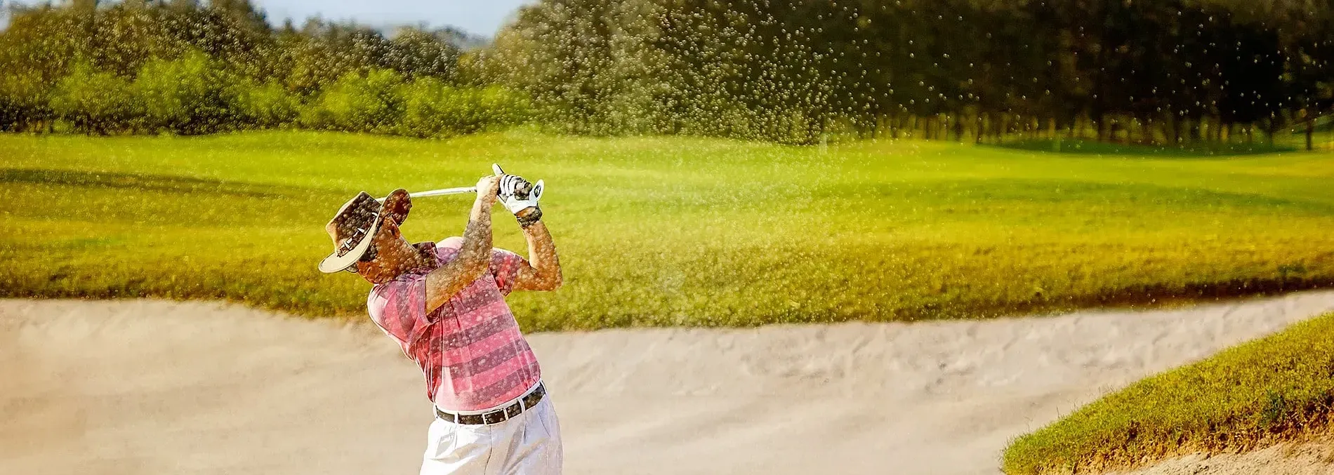 Golfer swinging a club in a sand bunker on a golf course surrounded by trees at Karma Chalets.