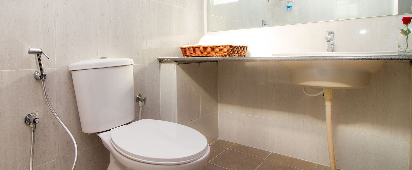 A bathroom featuring a toilet and a sink with tiled floor at Sanctum Suites Whitefield, Bangalore.