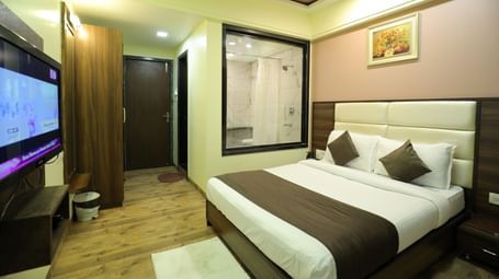 A bedroom at Krushnai Resort with a large TV, a king size bed, and a partial view of the bathroom through a glass wall.
