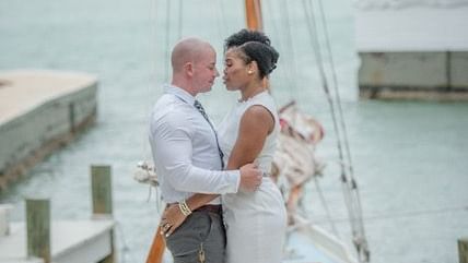 A couple hugging each other by the water with a sailboat mast visible in the distance. This beautiful scene is set at Casa Morada.