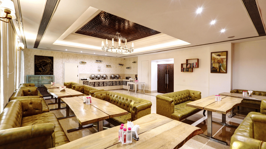 An inviting restaurant interior featuring green leather sofas paired with light wood tables and framed artwork on the walls - Flute Boutique By Hotel 91, Jaipur