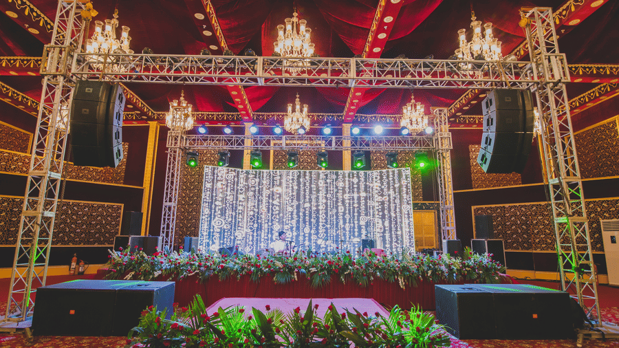A grand event stage at Rajasthali Resort & Spa, featuring a well-lit backdrop, floral arrangements, red drapes and ornate chandeliers, ideal for a marriage resort in Jaipur.