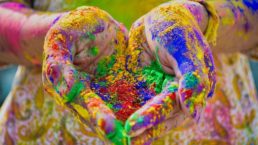 An image of a person holding powered colours in her hand which includes green, blue, red, and yellow during Holi celebration