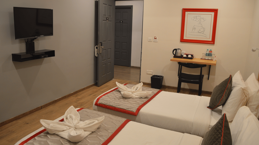 A bedroom featuring two single beds with a mounted television, and a framed artwork - Lords Eco Inn Belagavi