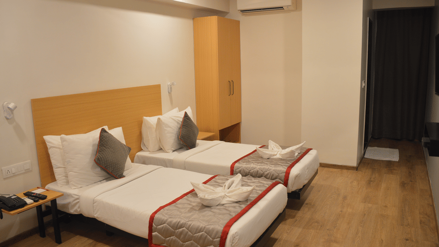 A bedroom with two single beds, air conditioning, and neutral decor - Lords Eco Inn Belagavi