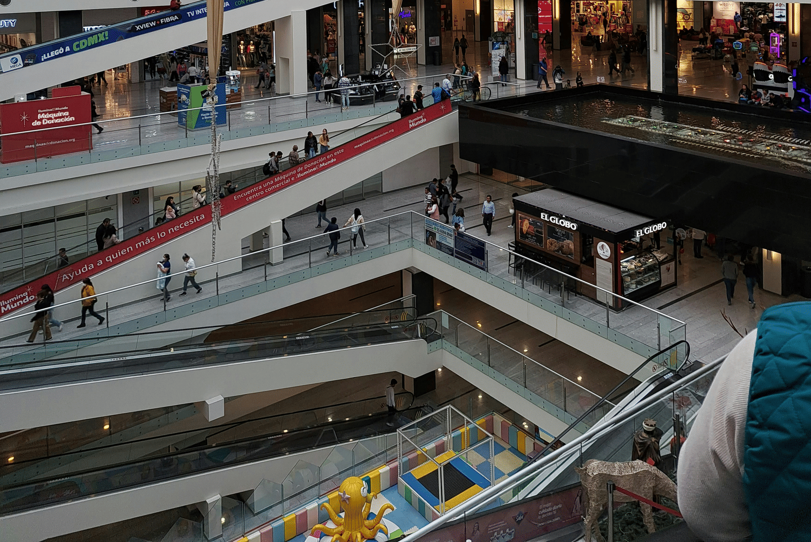 A large, multi-story shopping centre with escalators and many shops visible inside.