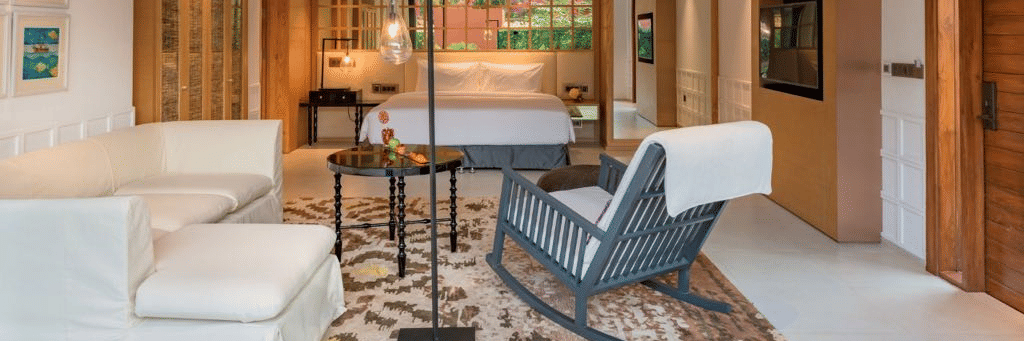 Villa room with a blue rocking chair and couches in front of a plush bed under warm lighting at Azaya Beach Resort in Goa with private pool