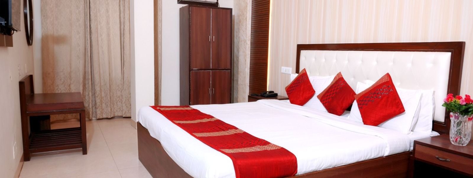 Comfortable double bed room at Hotel Diamond Inn, Chandigarh with red cushions , a wardrobe and a bedside table.