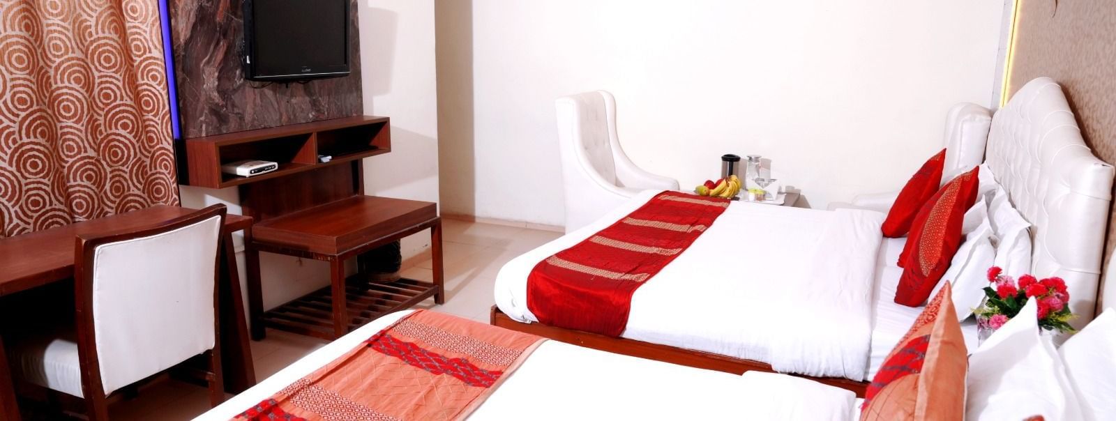 Two double-bedded rooms at Hotel Diamond Inn, Chandigarh, with bright red accents, flat-screen TVs and work tables.