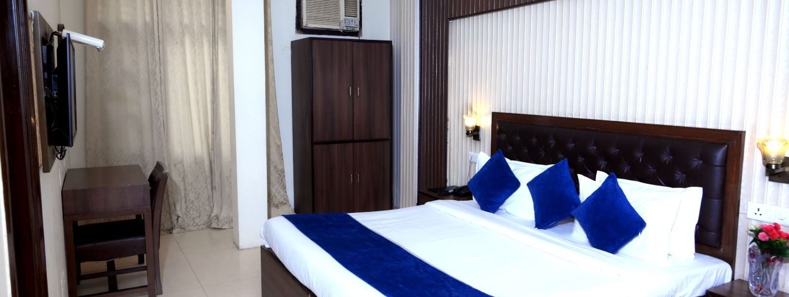 Neat hotel room at Hotel Diamond Inn, Chandigarh featuring king-size bed with blue wraps, a work desk, wooden wardrobe and bedside table.