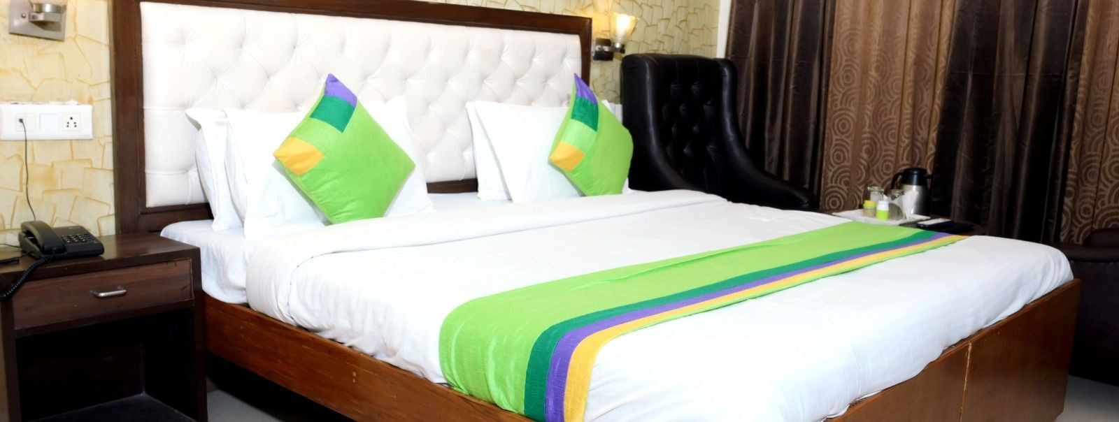 Brightly furnished king-size bedded room with blue and green pillows and well-lit decor at the Hotel Diamond Inn in Chandigarh.