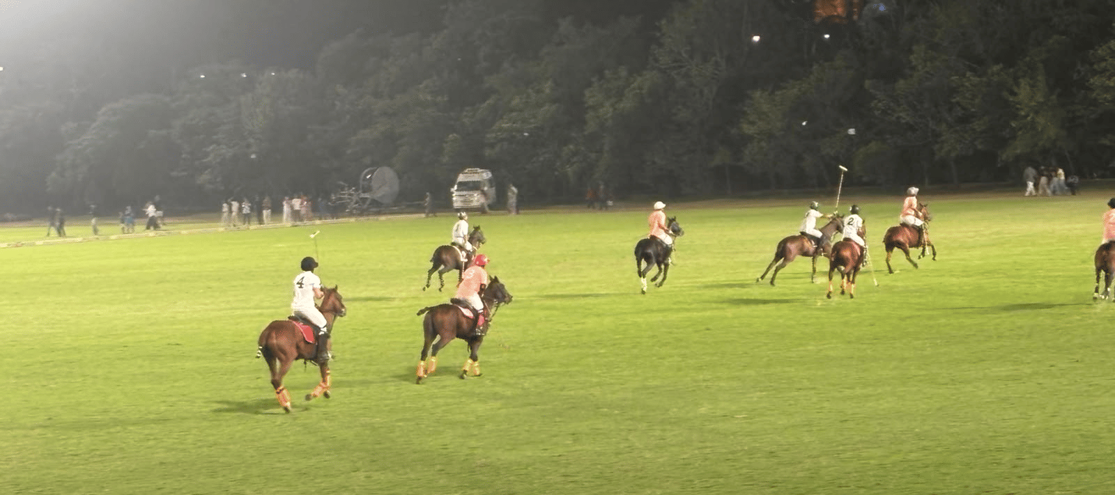 Polo players scattered across a expansive green field under bright stadium lights during the Jaipur Polo Season.