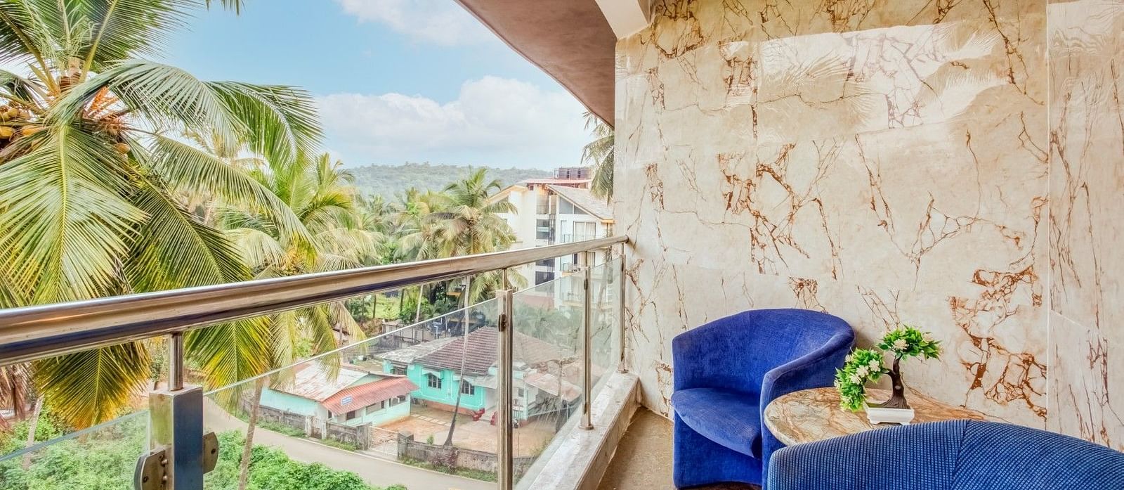  Balcony with a two-seater cushioned sofa and a table positioned in the centre, offering a view of the coconut trees