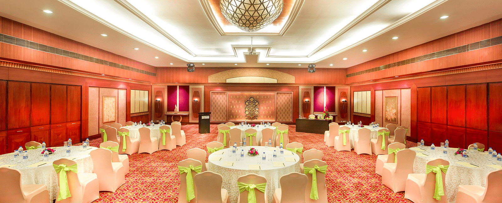 A wedding hall with white chairs tied with yellow ribbons pointing towards the stage at Grand Chennai By GRT Hotels.