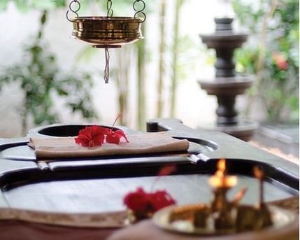 Ayurvedic spa setup with herbal oils, flowers, and traditional vessels in an open garden setting.