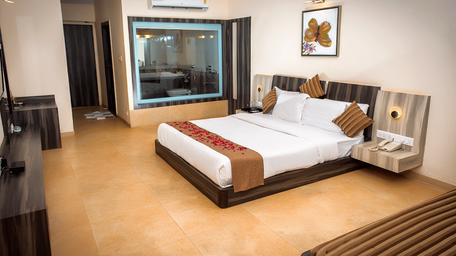 A view of the bed in Regency Room with its two side tables, glass window to the bathroom, diwan, and a consoel.