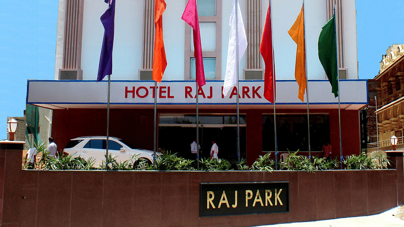Facade of Raj Park hotel with blue sky in the background and a car parked in the entrance of the hotel