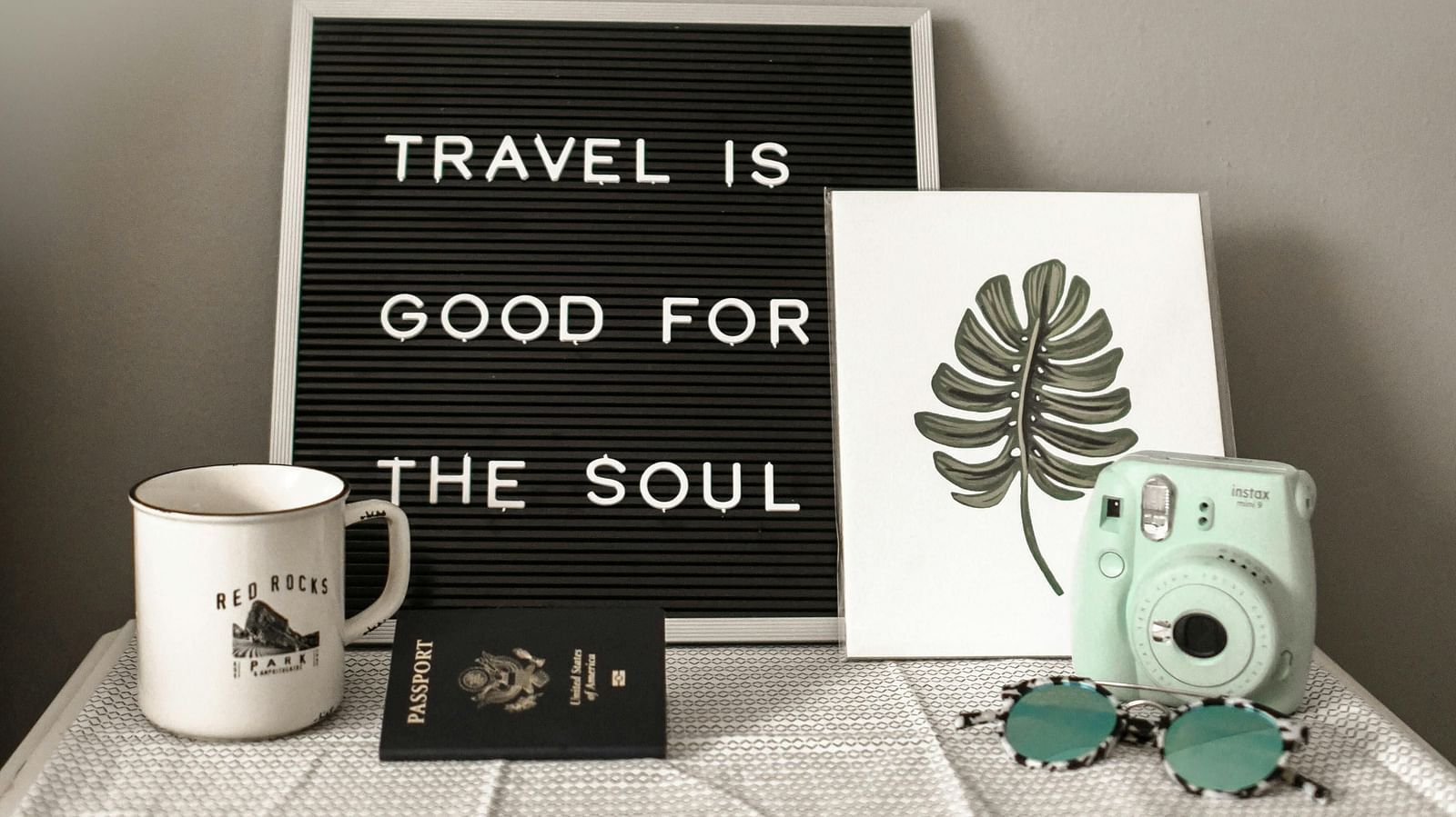  A quote board reading travel is good for the soul placed beside a plant and a coffee cup.