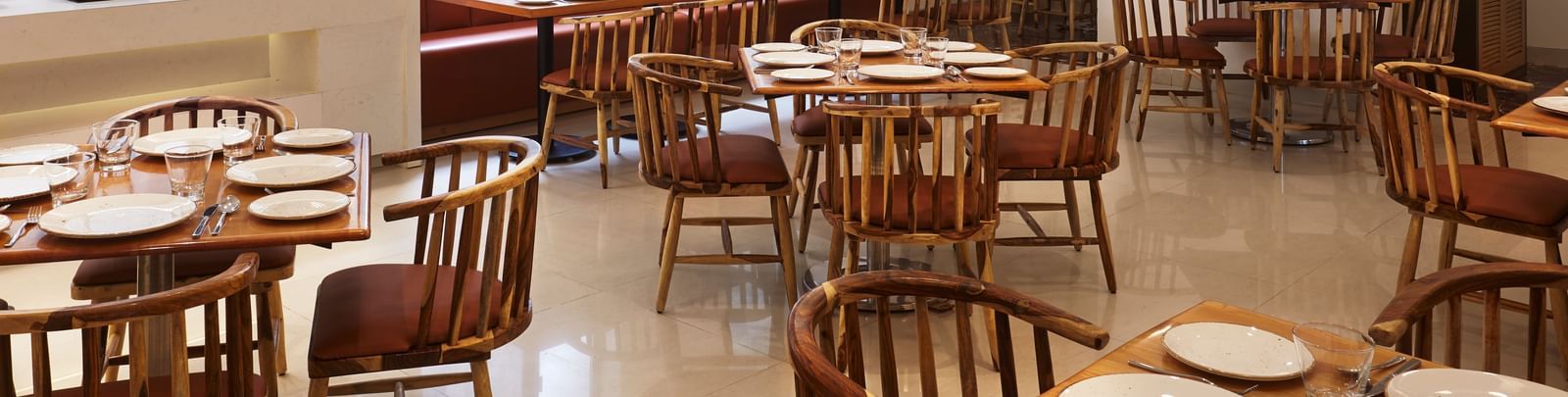 A spacious, modern dining hall at Monday Hotels Mahape, Navi Mumbai, with multiple wooden tables, chairs, and a long booth.