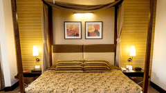 A bedroom with a four-poster bed, two side tables with lamps, framed wall art, and warm lighting.