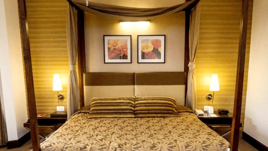 A bedroom with a four-poster bed, two side tables with lamps, framed wall art, and warm lighting.