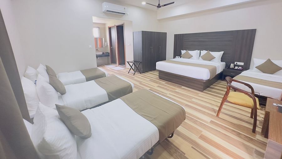 A room contains double beds with grey and white bedding, a seating area, and a ceiling fan - Kankidham Lords Inn