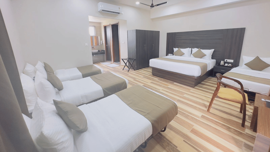 A room contains double beds with grey and white bedding, a seating area, and a ceiling fan - Kankidham Lords Inn