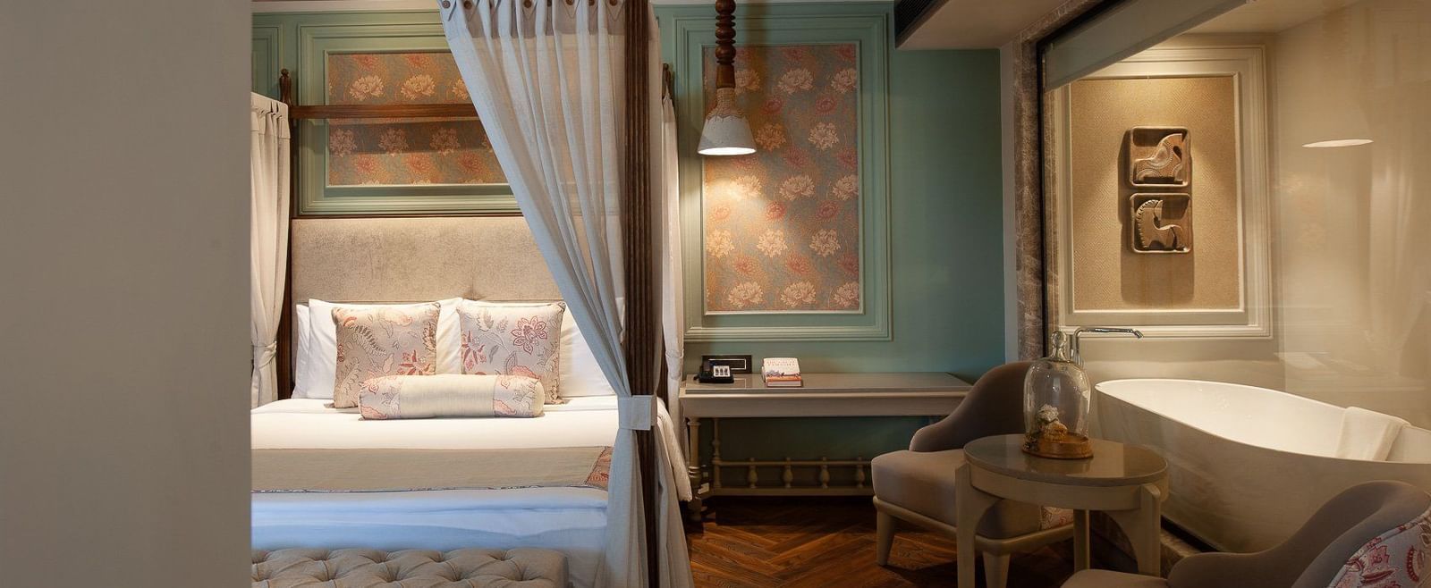 A serene corner of a suite at The Evren, Vagator, showing the four-poster bed and a glimpse of the luxurious bathroom with a freestanding bathtub visible through a glass partition.