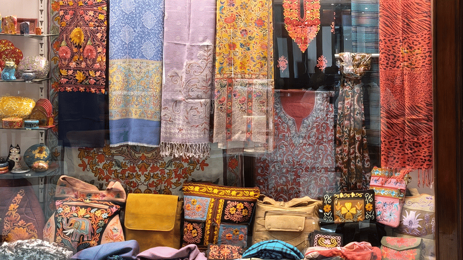 A close-up of a display case containing embroidered bags and hanging silk fabrics in various colours | HHI Varanas