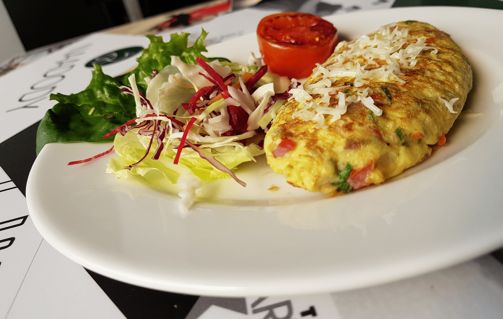 A plate of omelette with a side salad. The omelette is golden brown and filled with vegetables. The salad is green and includes tomatoes and other vegetables.