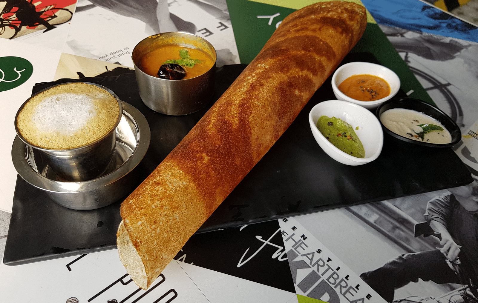 Masala dosa with chutney, sambhar and a side of coffee kept on a black plate
