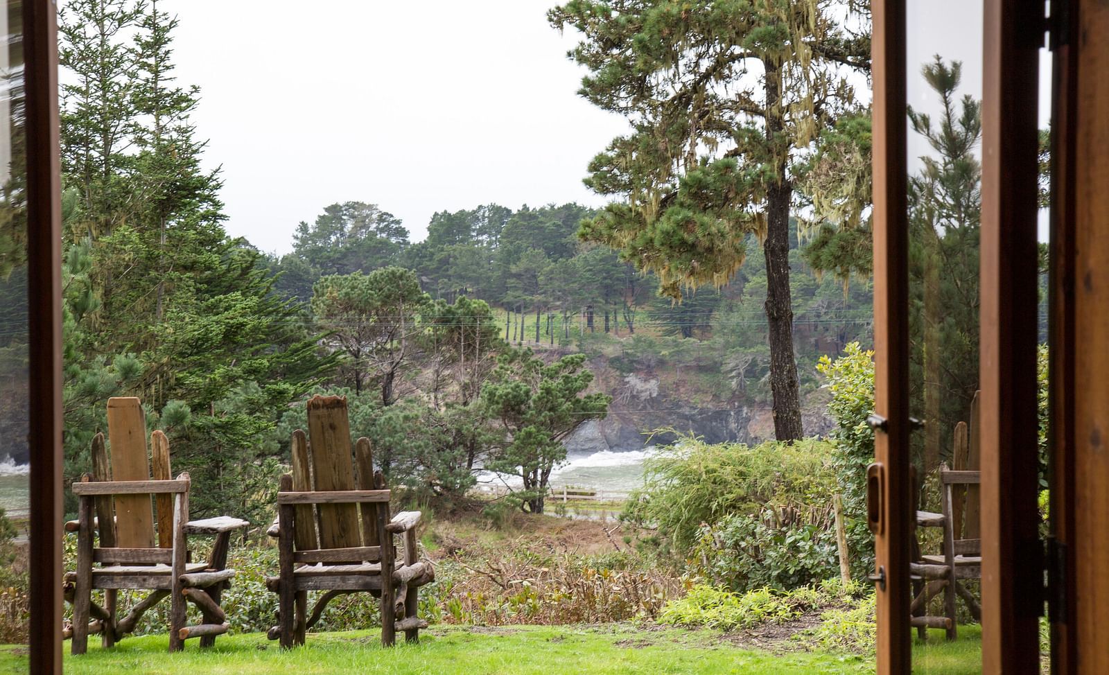 A view of two cozy wooden chairs placed on a well manicured lawn from the window of our hotel room - Brewery Gulch Inn & Spa