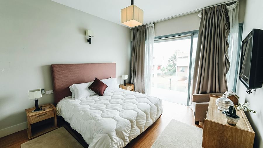 A  bedroom with a stylish ceiling light, a large window draped with curtains.