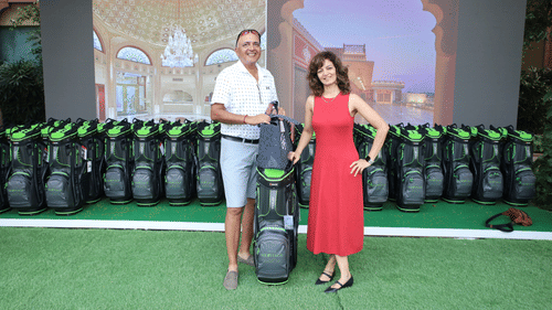 Golf event with a backdrop featuring branding and participants holding golf bags