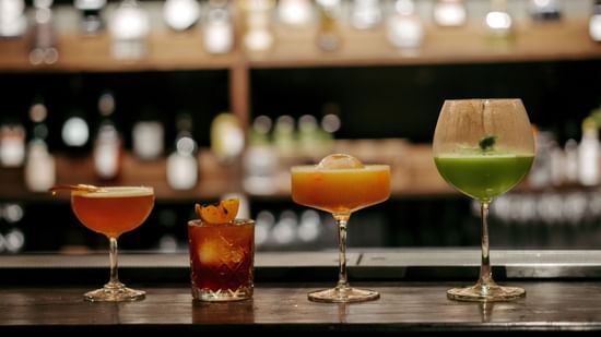 Four cocktails on a bar counter, blurred bottles in background.