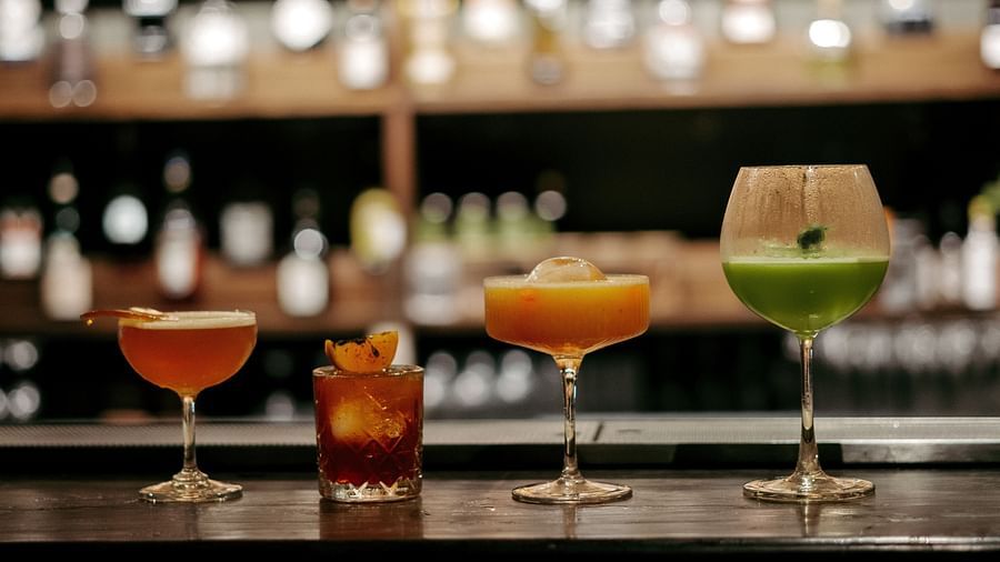 Four cocktails on a bar counter, blurred bottles in background.