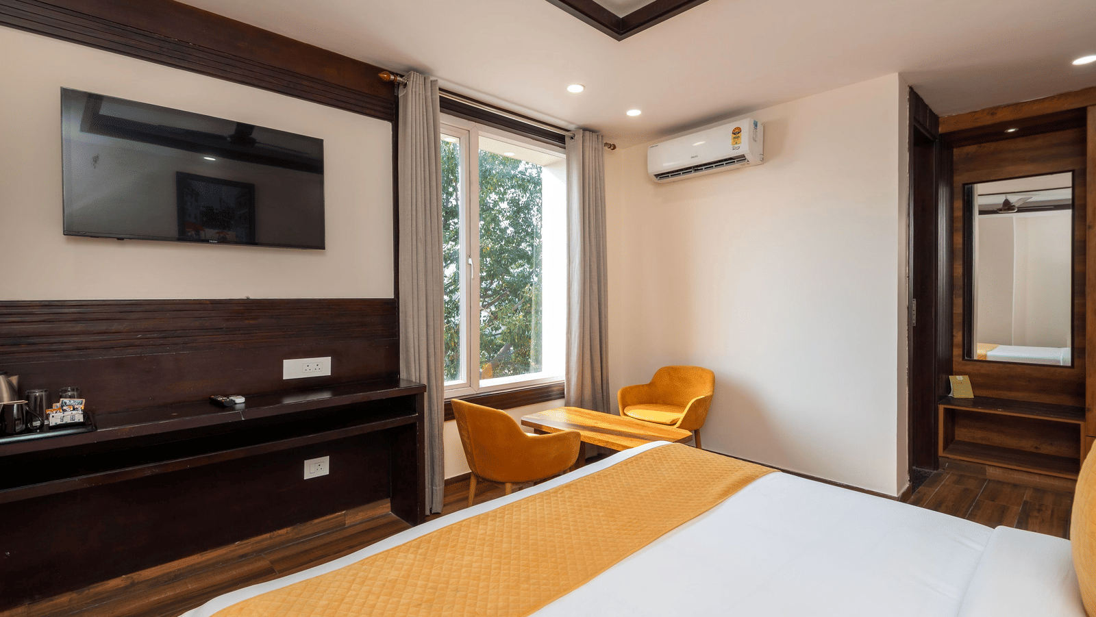 View from the bed showing a television mounted on the wall, and a window at Perfectstayz Premium Shanti Heritage, Haridwar.