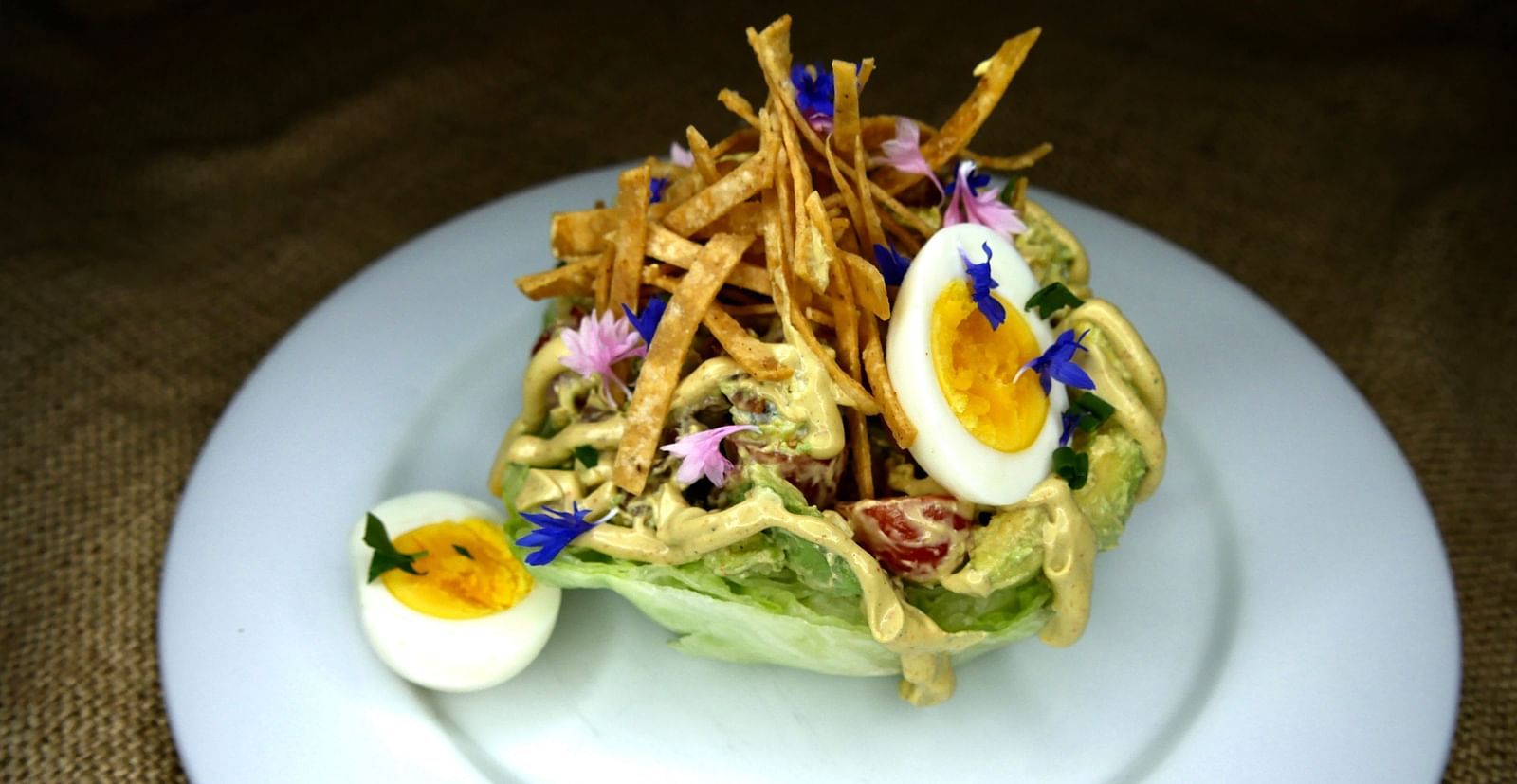 A plated salad at Shaver Lake Village Hotel with crisp toppings, a boiled egg, and edible flowers, served on a textured background.